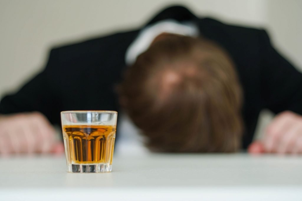 man with his head on the table with alcohol in front of him